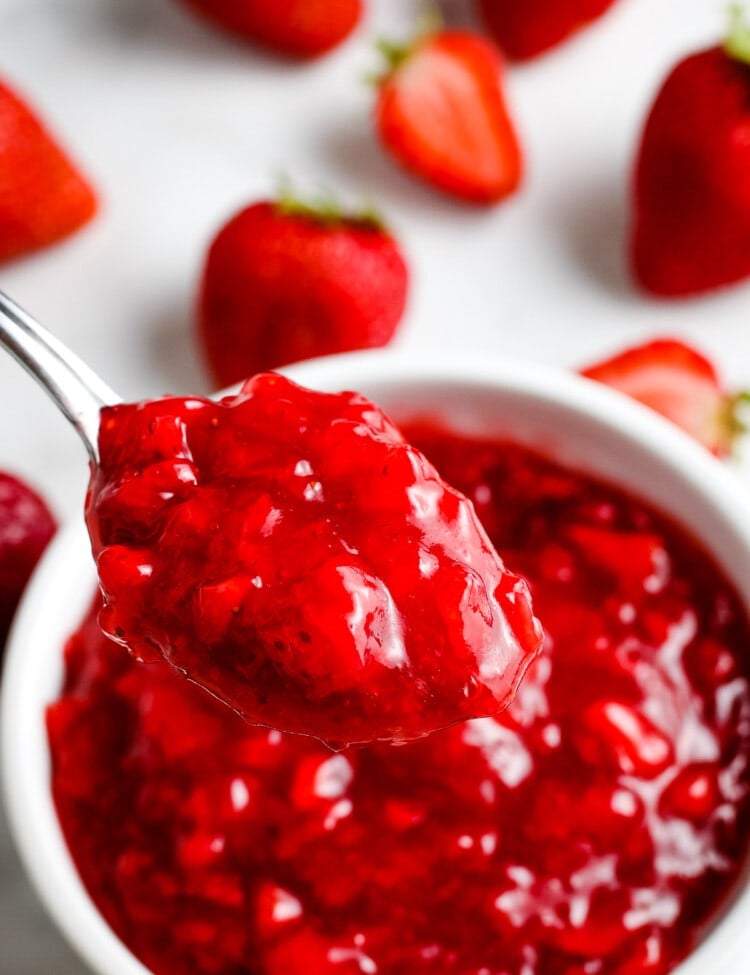 Spoon with a scoop of strawberry sauce on it with more in a bowl in background