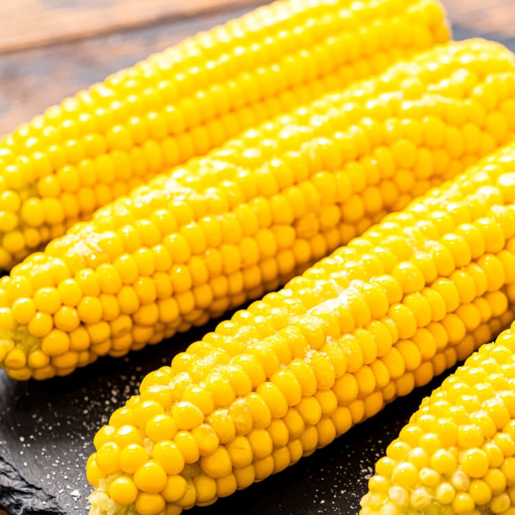 Four pieces of corn on the cob laying on a round piece of slate.