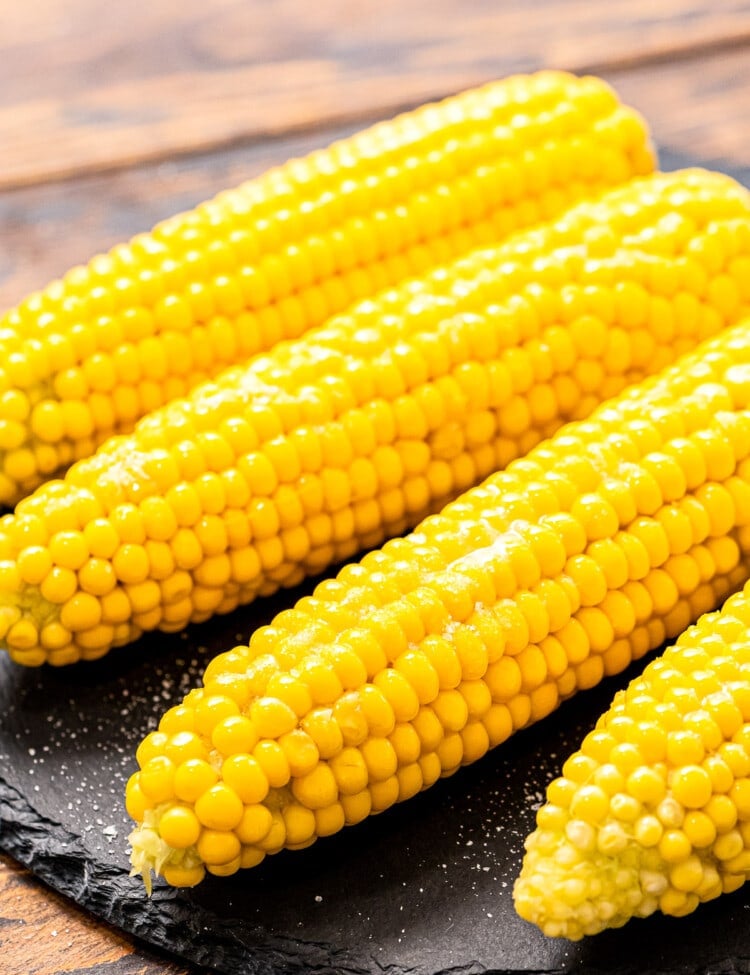 Four pieces of corn on the cob laying on a round piece of slate.