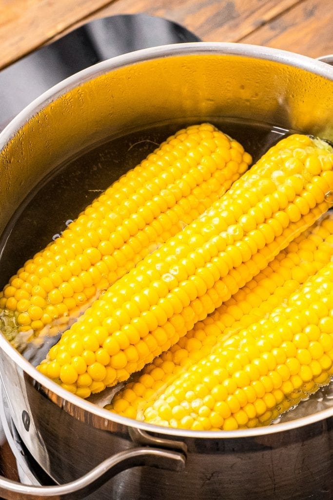 A pot with corn on the cob and water in it.