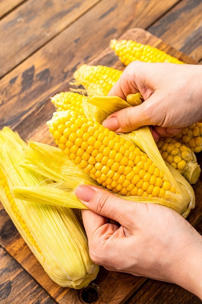 Hands husking corn on the cob after it's been cooked.