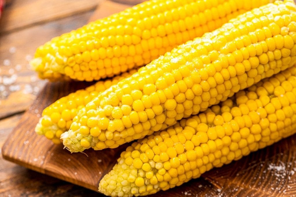 Piece of corn on the cob on a wood cutting board.