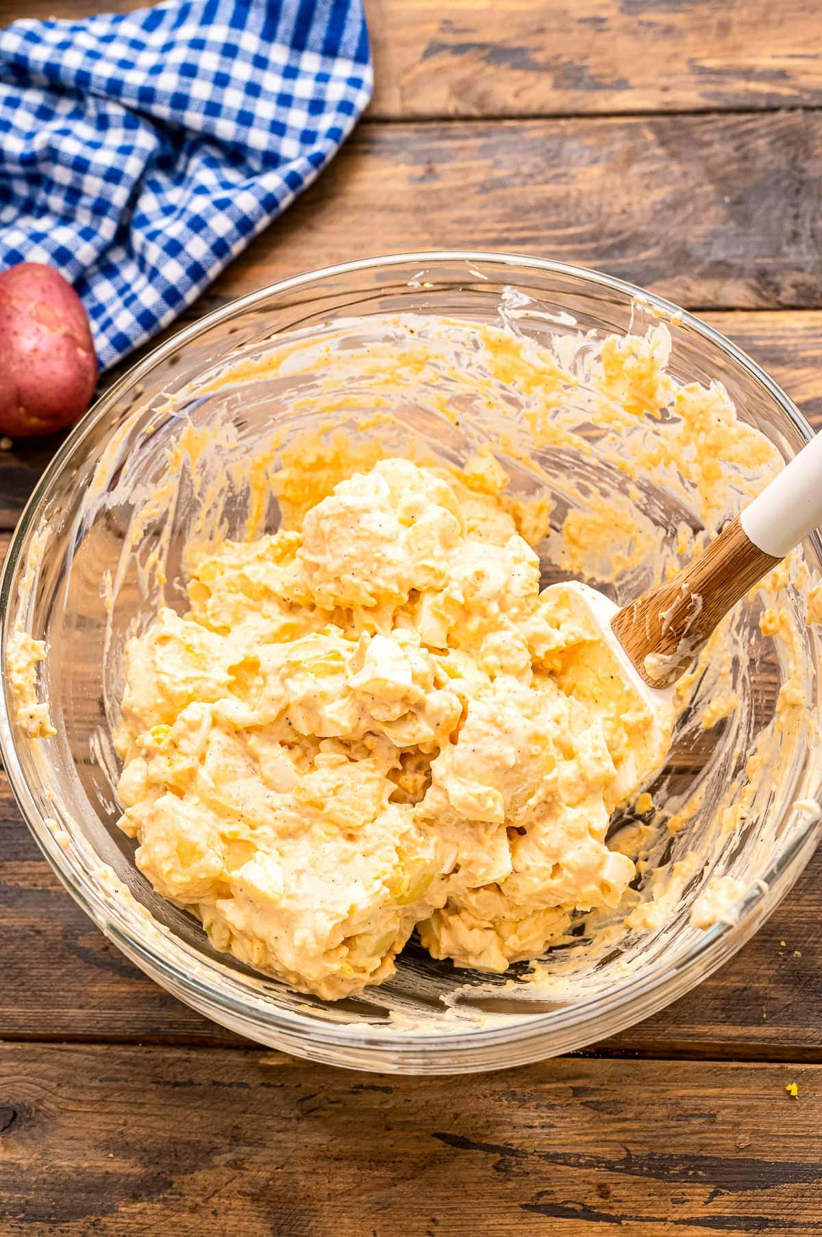 Bowl of potato salad being mixed together on a wooden background