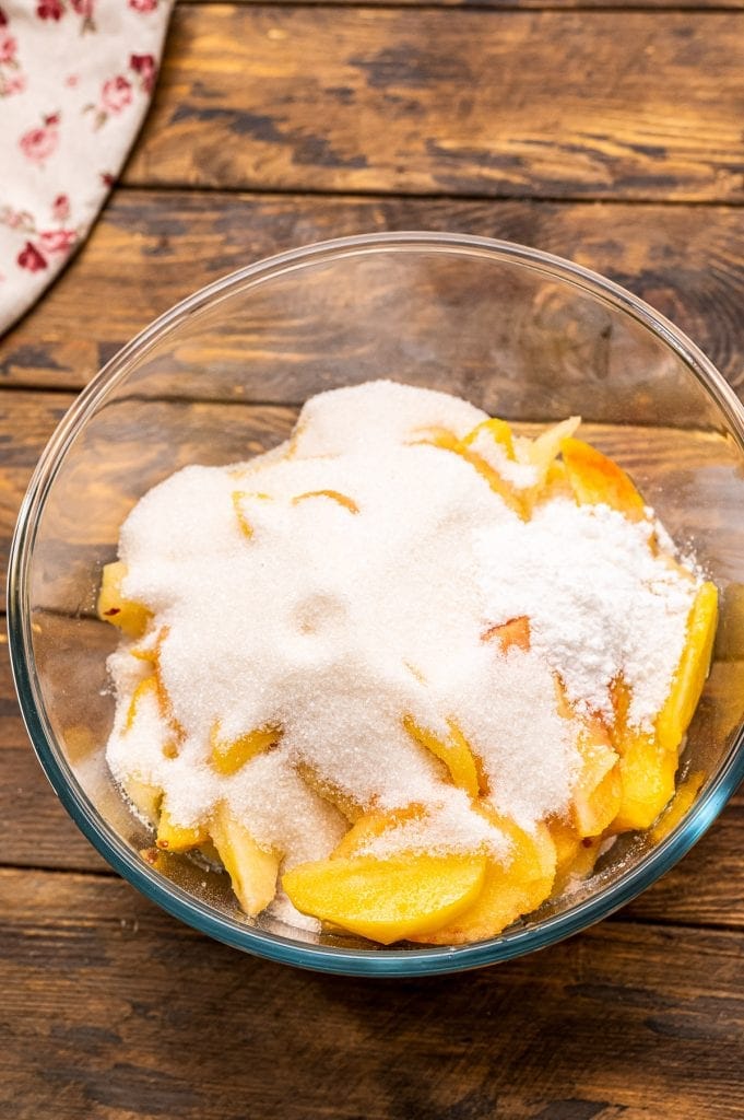 Glass bowl with fresh sliced peaches on bottom and sprinkled with sugar and tapioca.