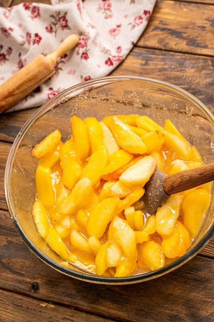 Bowl of fresh peaches mixed with sugar and tapioca on a wooden background