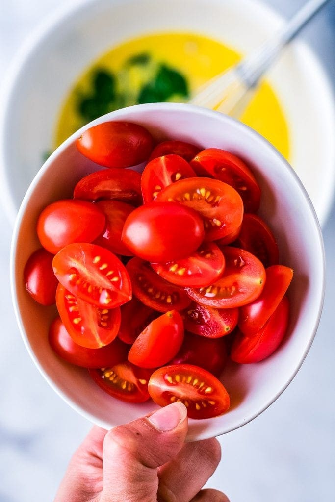 Hand holding white bowl with halved tomatoes