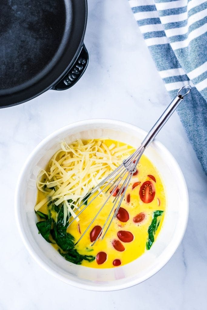 White bowl with whisk and ingredients for frittata in it