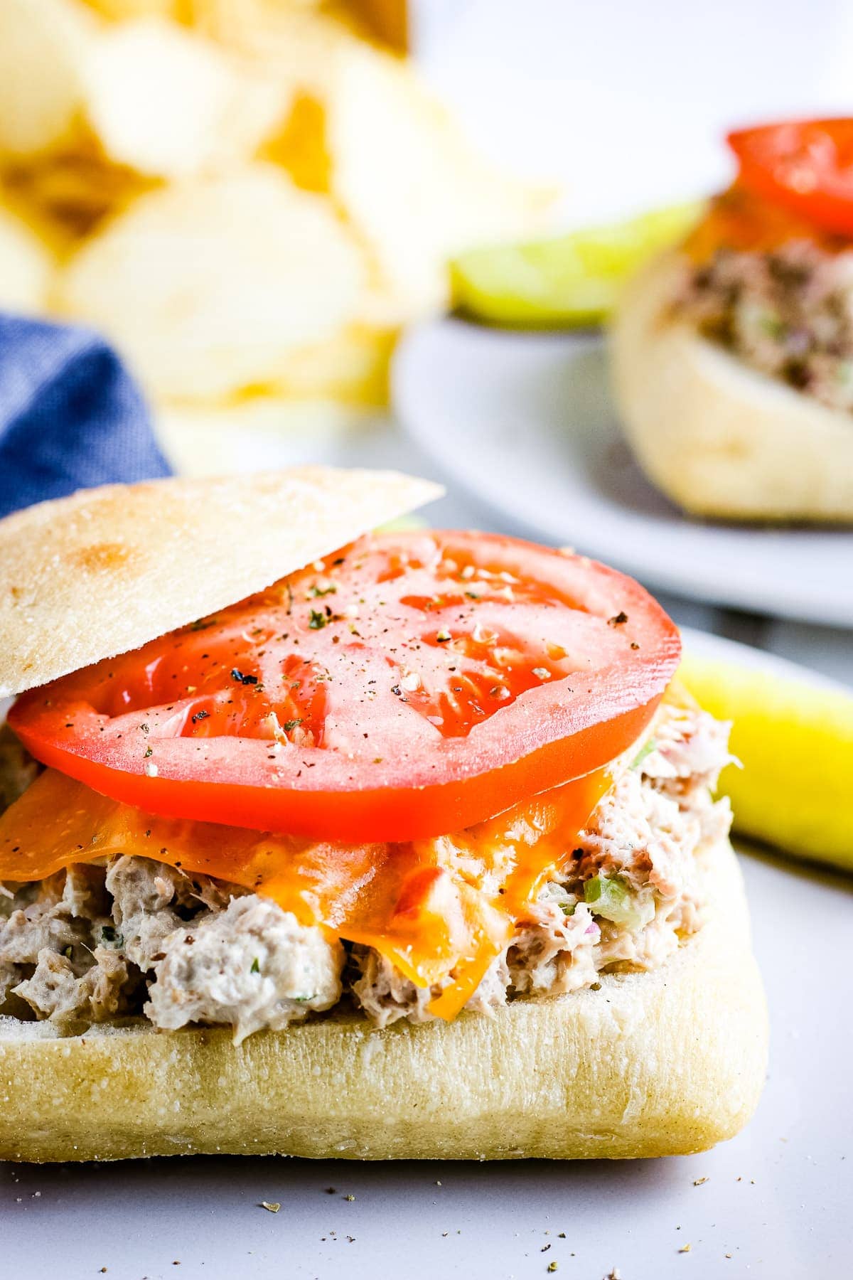 A sandwich topped with tuna filling, cheese slice and tomato slice