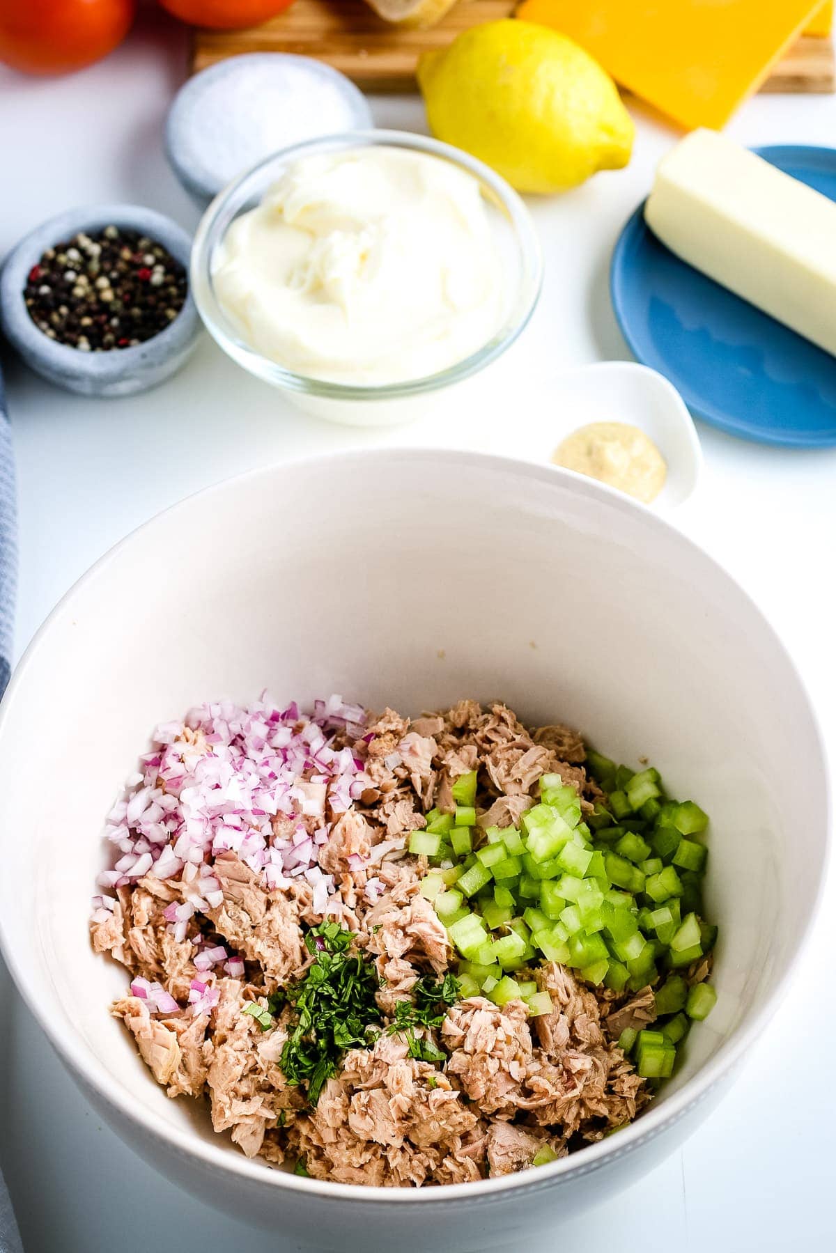 White mixing bowl with tuna, celery, re onion and parsley.