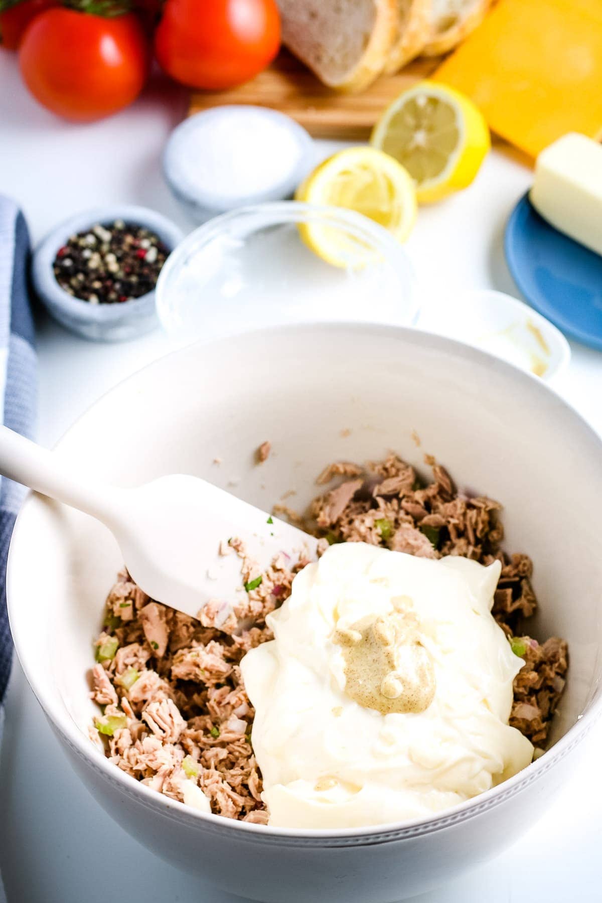 White bowl with with tuna, celery, re onion and parsley mixed together and amyonnais, mustard and lemon juice on top.