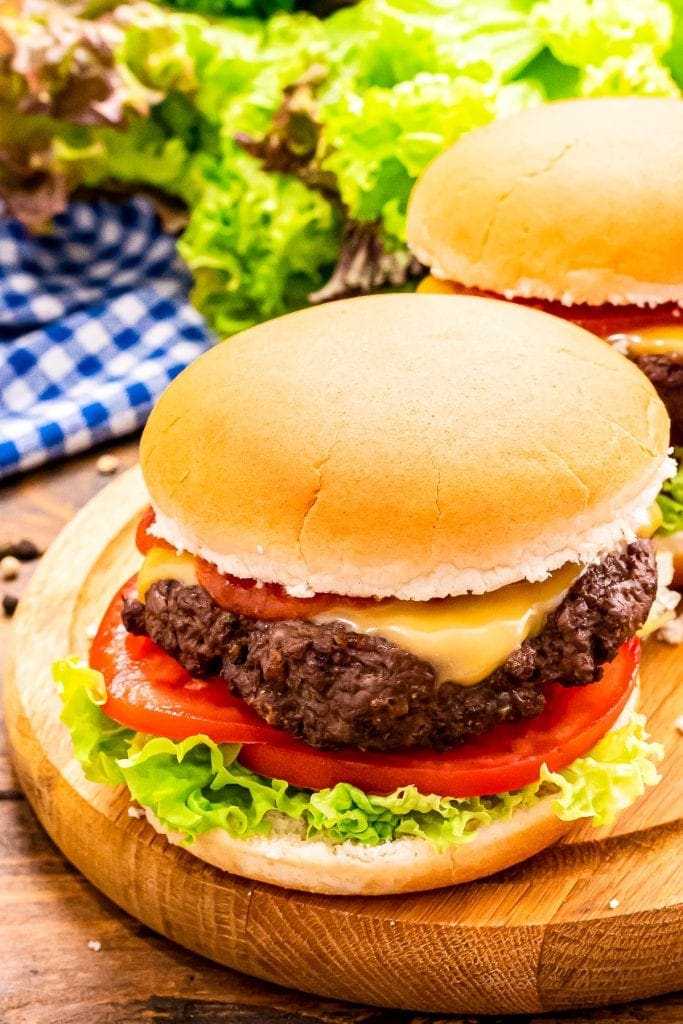 Wood platter with a burger in a bun topped with cheese, lettuce and tomato