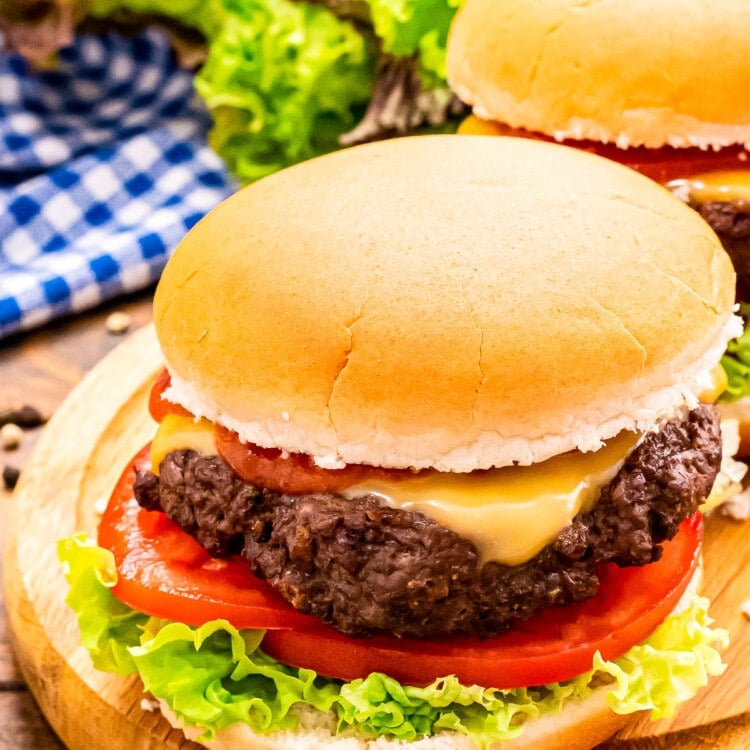 Wood platter with a burger in a bun topped with cheese, lettuce and tomato