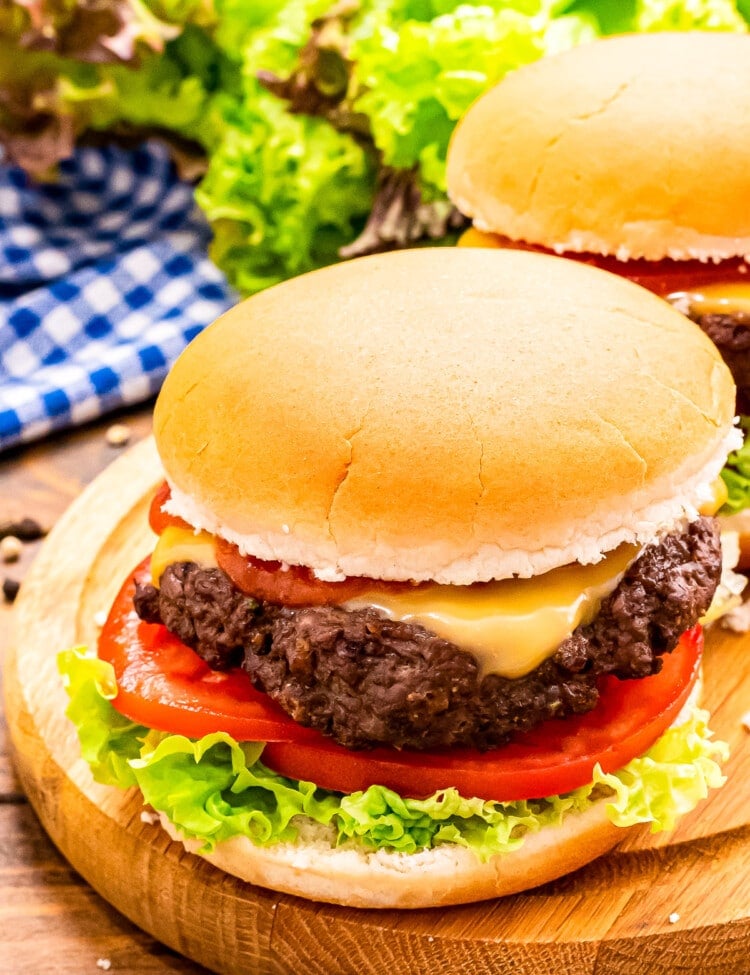 Wood platter with a burger in a bun topped with cheese, lettuce and tomato