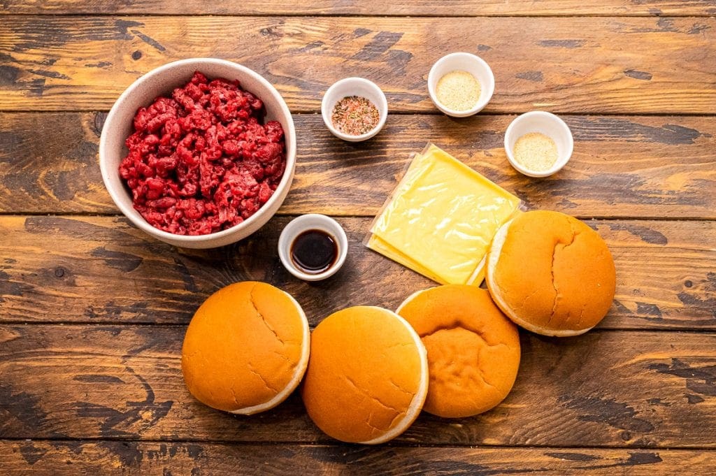 Wood background with ingredeints for hamburgers in small bowls like ground beef, buns, cheese slices and seasonings