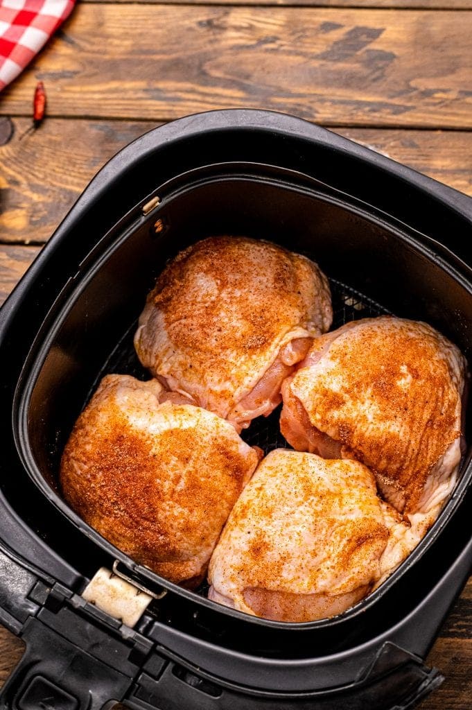 Air Fryer basket with 4 seasoned raw chicken thighs in it