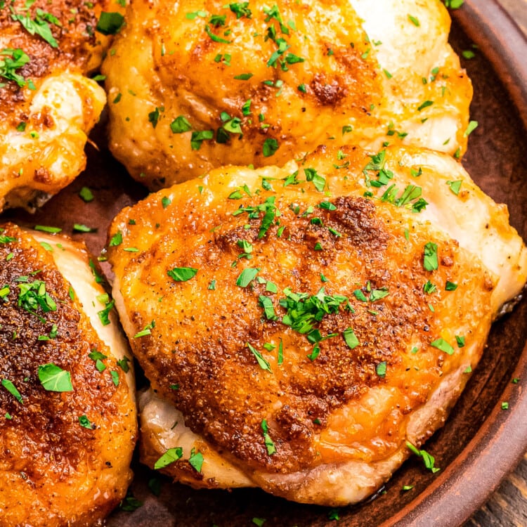 Brown plate with cooked chicken thighs on it garnished with fresh parsley