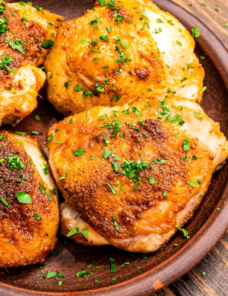 Brown plate with cooked chicken thighs on it garnished with fresh parsley