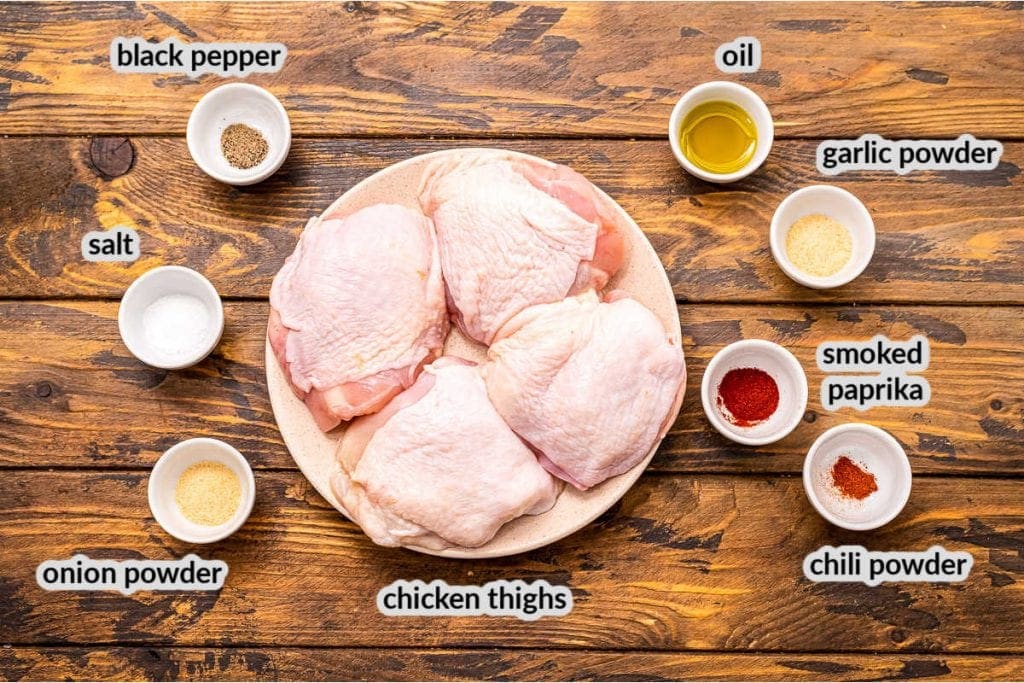 Overhead image of ingredients for Air Fryer Chicken Thighs including seasonings, oil and chicken thighs in bowls or plate respectively
