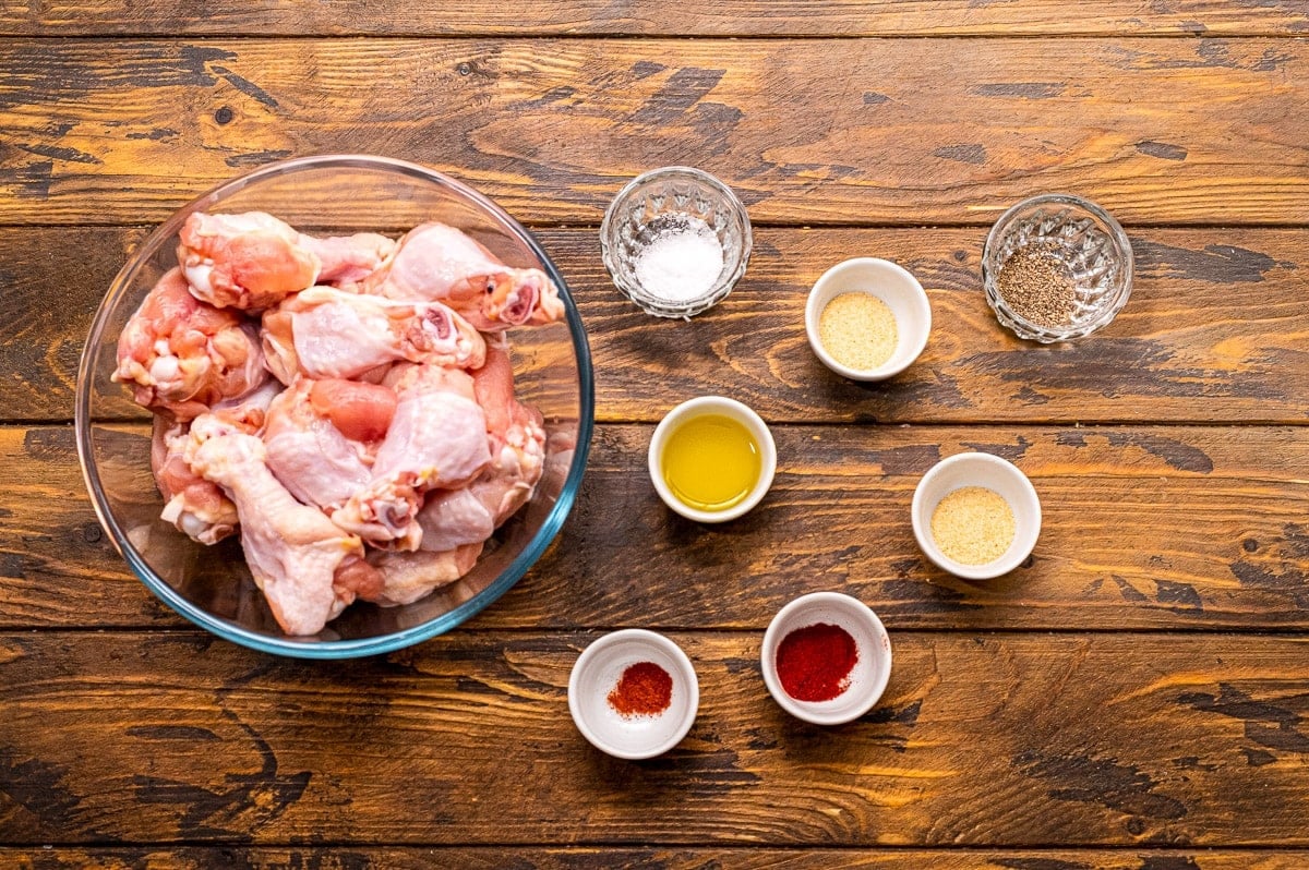 Overhead image of ingredients including a bowl of chicken wings, seasonings in multiple bowls and olive oil in a bowl