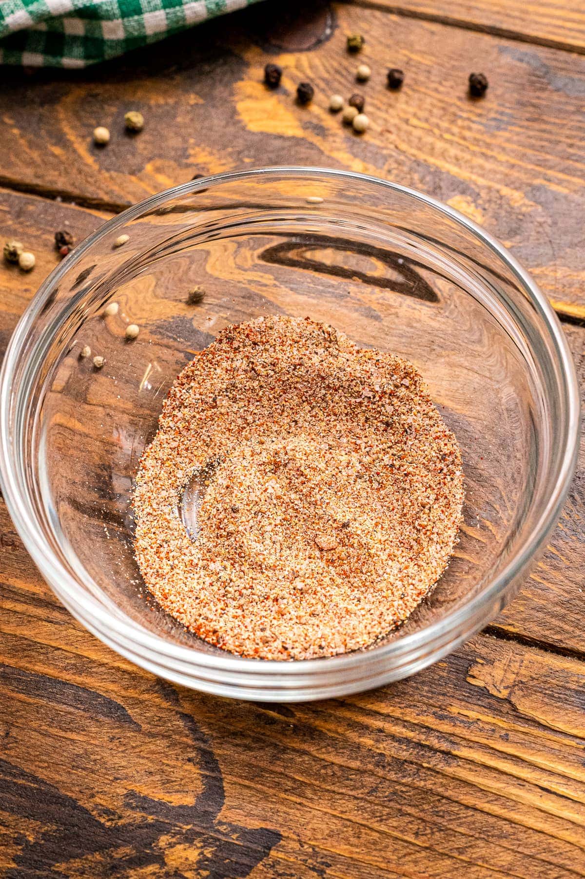 Glass bowl with seasonings mixed up in it on a wood board.