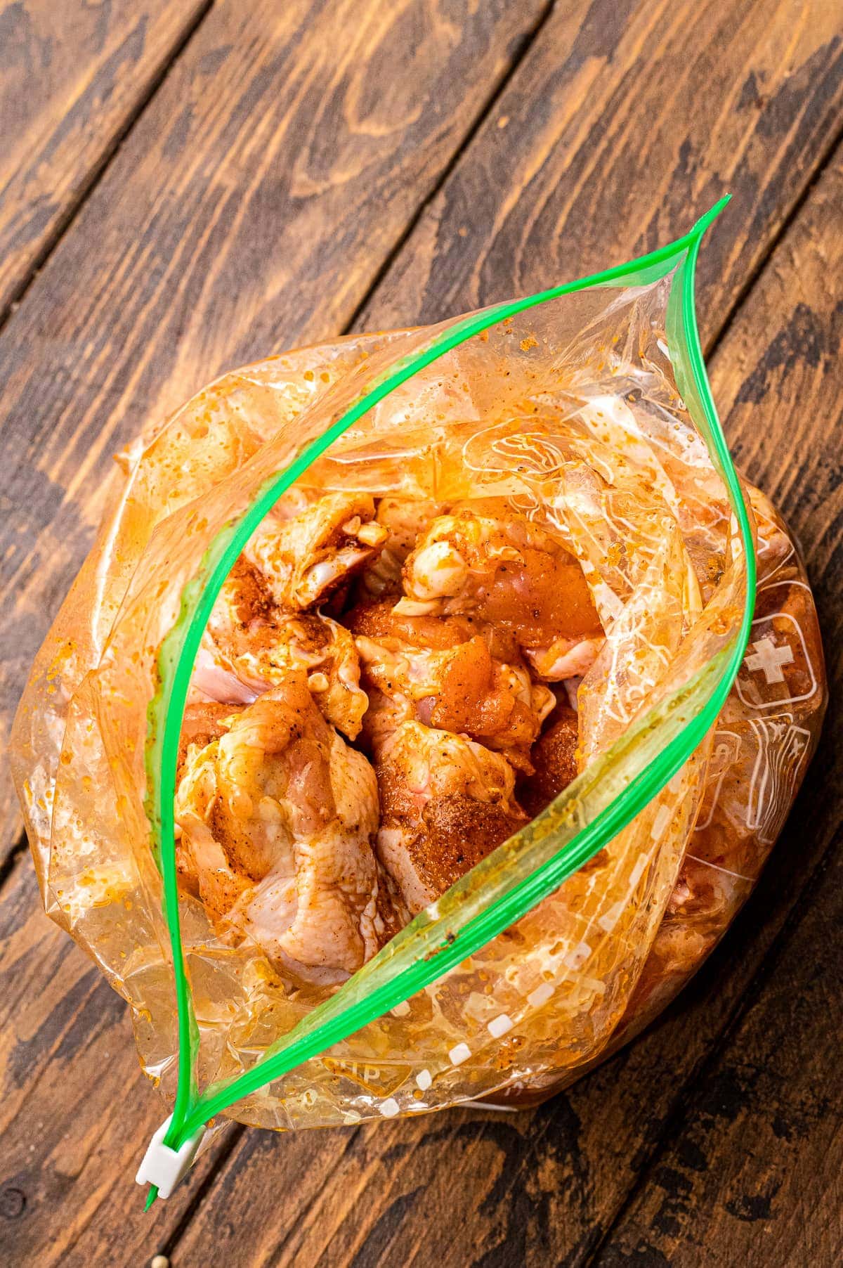 Ziplock bag with chicken wings in it and seasonings on wood cutting board.