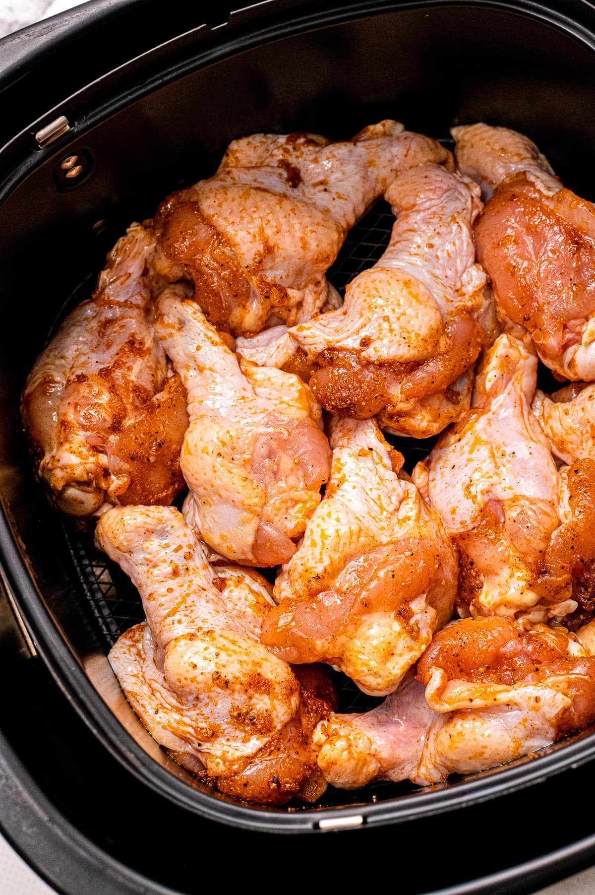 Air fryer basket with seasoned chicken wings.