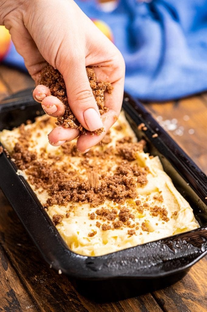 Hand sprinkling streusel over bread batter in loaf pan