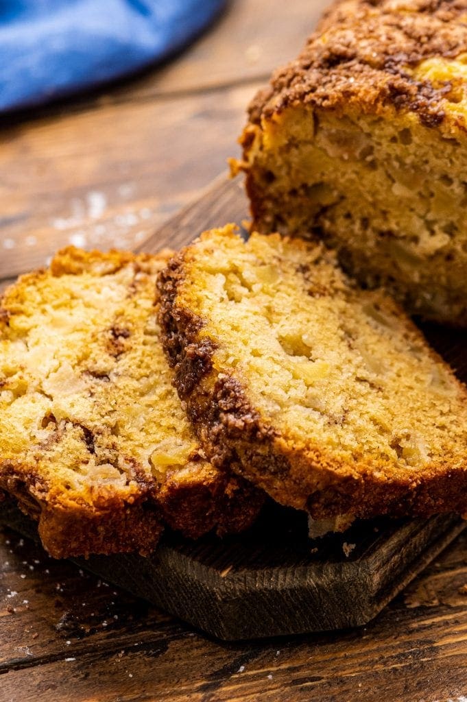 Two slices of apple bread next to the rest of the loaf on wood cutting board.
