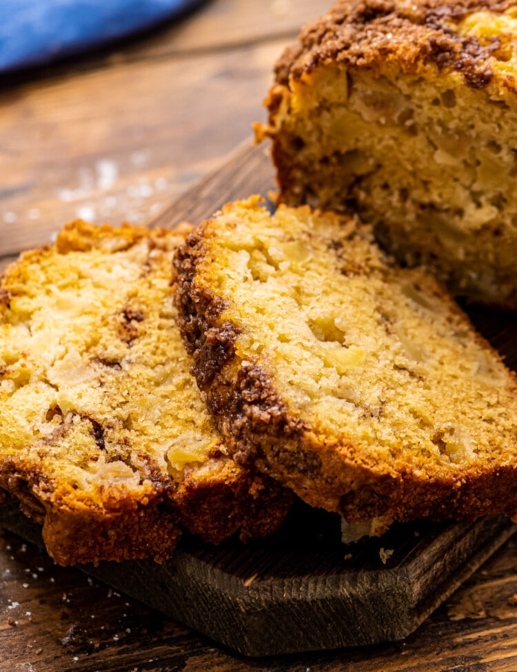 Two slices of apple bread next to the rest of the loaf on wood cutting board.