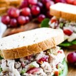 Close up image of sandwich filled with chicken salad and lettuce. Grapes and another sandwich in background.