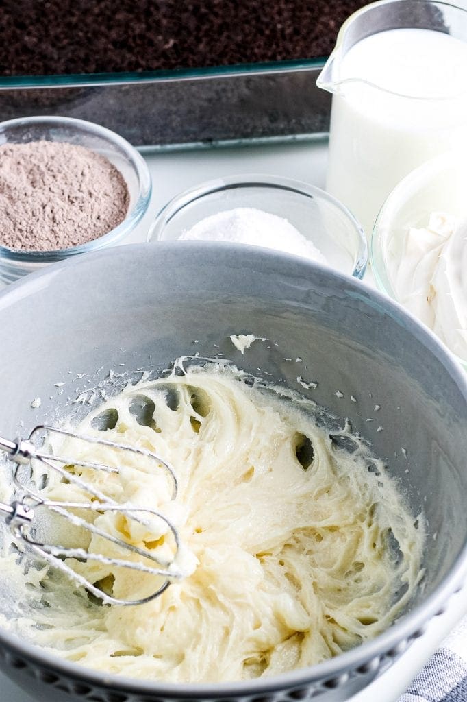 Gray bowl with cream cheese blended with sugar and hand mixer in it.