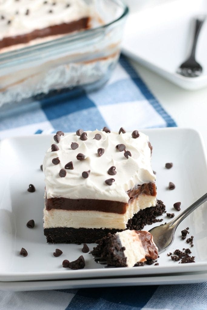 Square white dish with a piece of No Bake Chocolate Lasagna. A fork with a bite on it laying next to it.