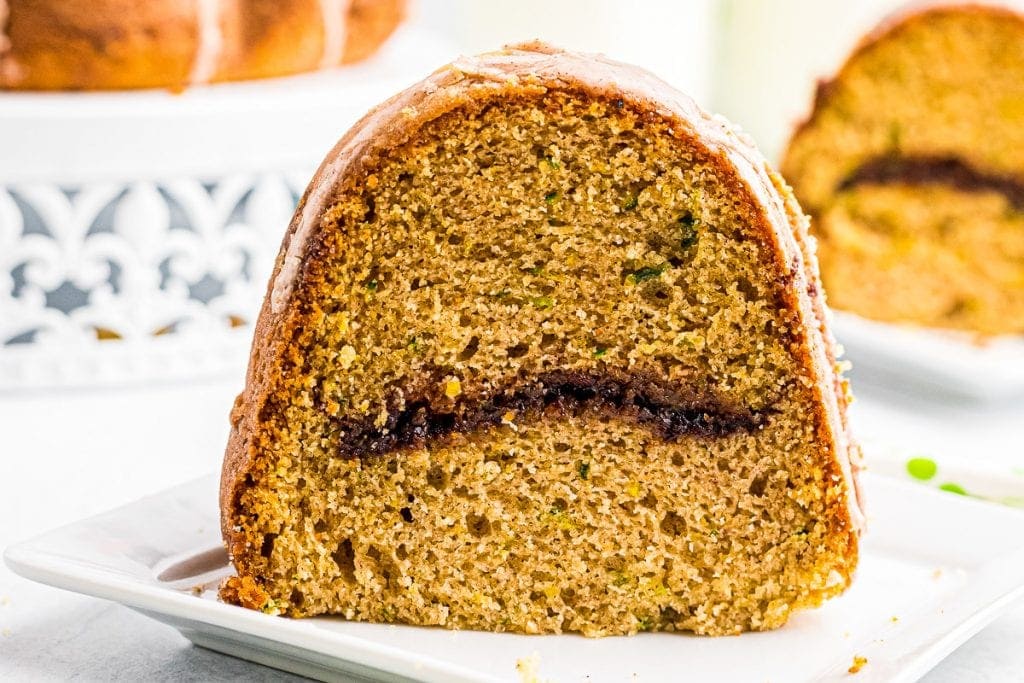 Slice of Zucchini Bundt Cake with a cinnamon layer in the middle on a white plate.