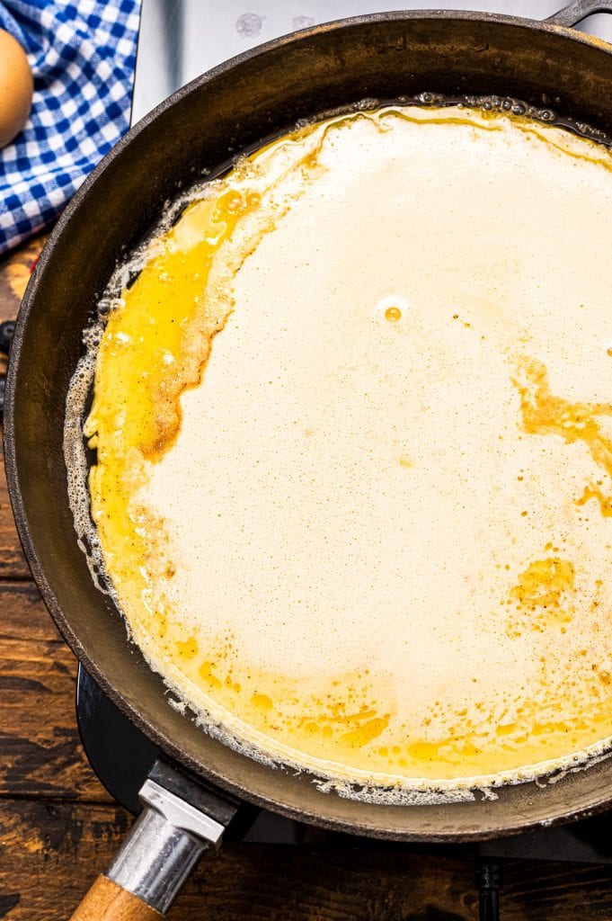 Cast iron skillet with batter in it and topped with melted butter.