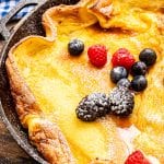 Cast Iron skillet with baked Dutch Baby Pancake topped with fresh berries in powdered sugar.