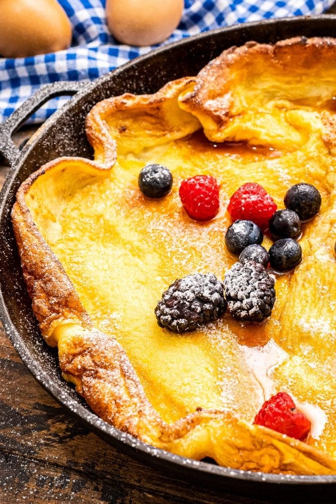 Cast Iron skillet with baked Dutch Baby Pancake topped with fresh berries in powdered sugar.