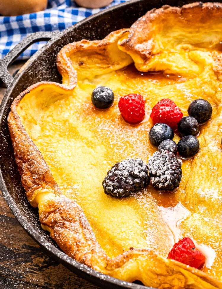 Cast Iron skillet with baked Dutch Baby Pancake topped with fresh berries in powdered sugar.