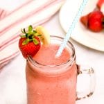 Mason Jar Mug with Strawberry Bananas Smoothie in it. Garnished with a blue and white striped paper straw, strawberry and banana slice on rim.