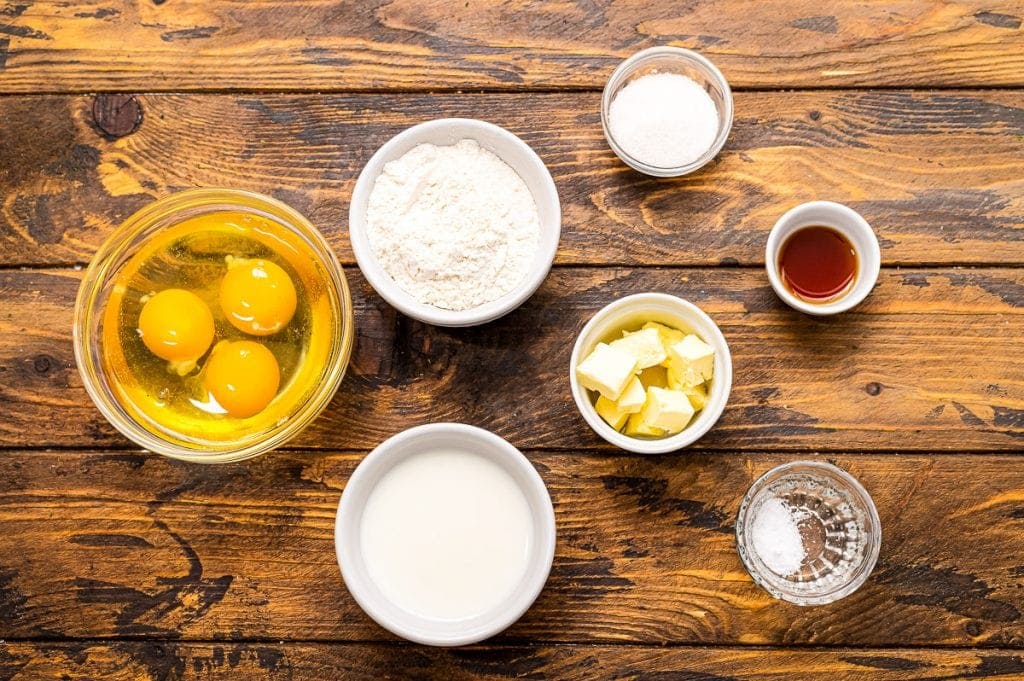 Ingredients in bowls including eggs, milk, butter, vanilla, sugar etc.