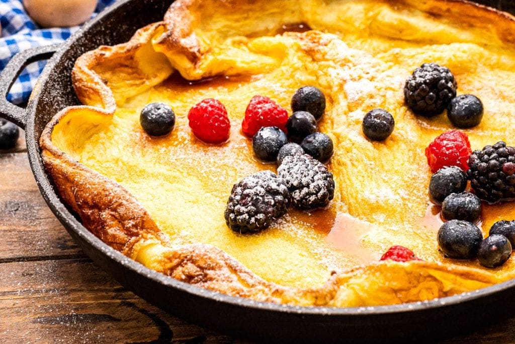 Close up image of baked Dutch Baby Pancake that's topped with berries and powdered sugar dusting.