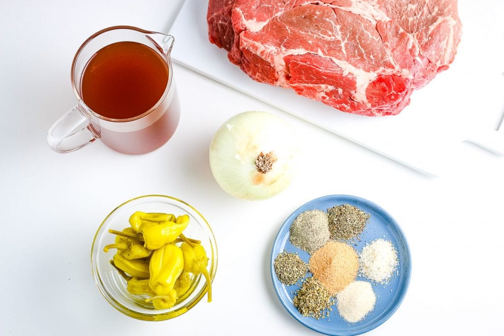 White Background with roast, seasonings, onion, beef broth and pepperoncini peppers for recipe