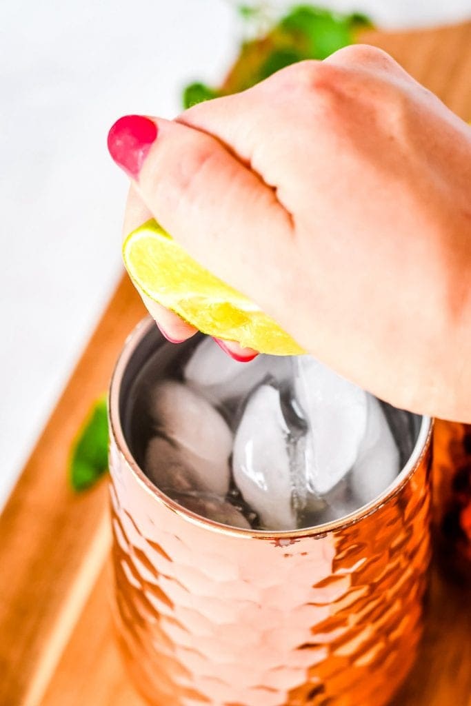 Hand squeezing lime into a copper glass with ice cubes.