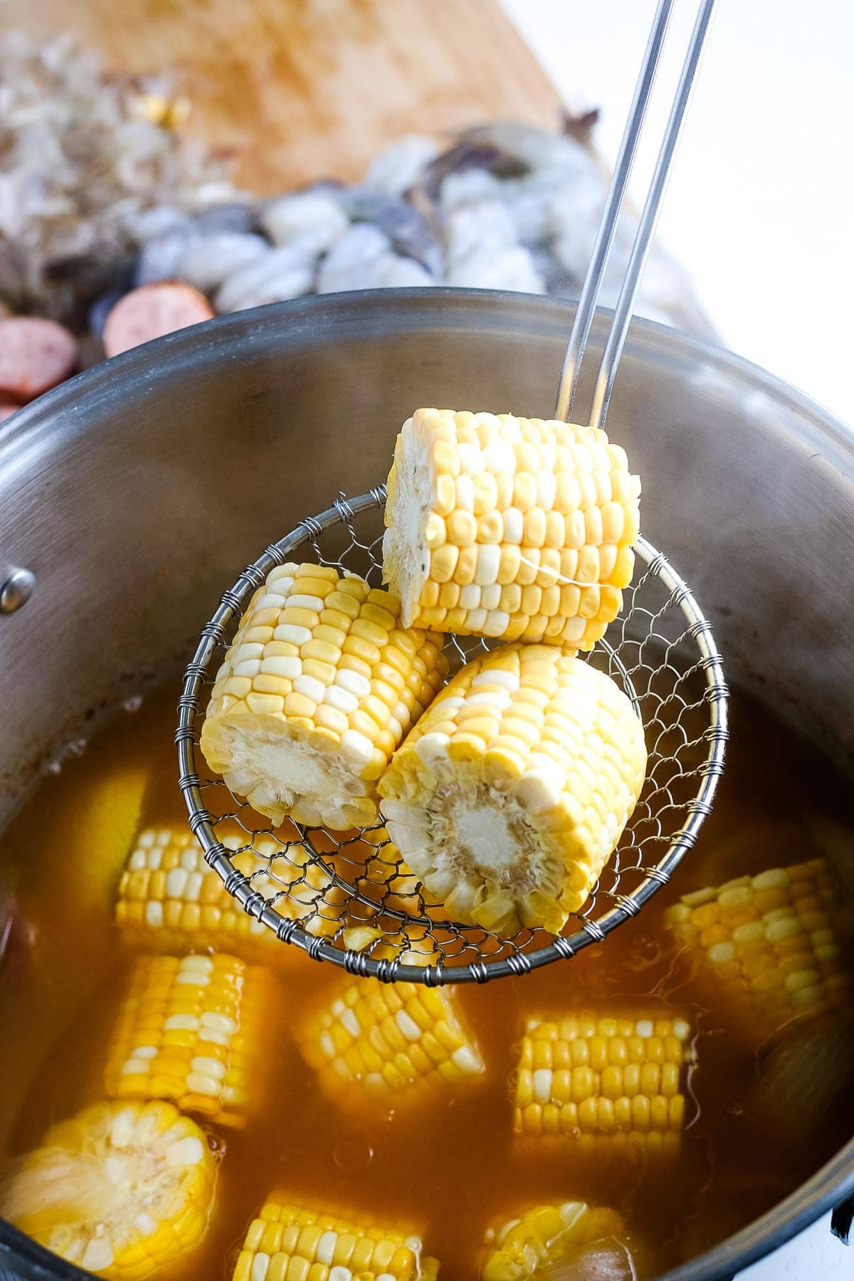 Ladle holding small pieces of corn on the cob before putting it into shrimp boil.