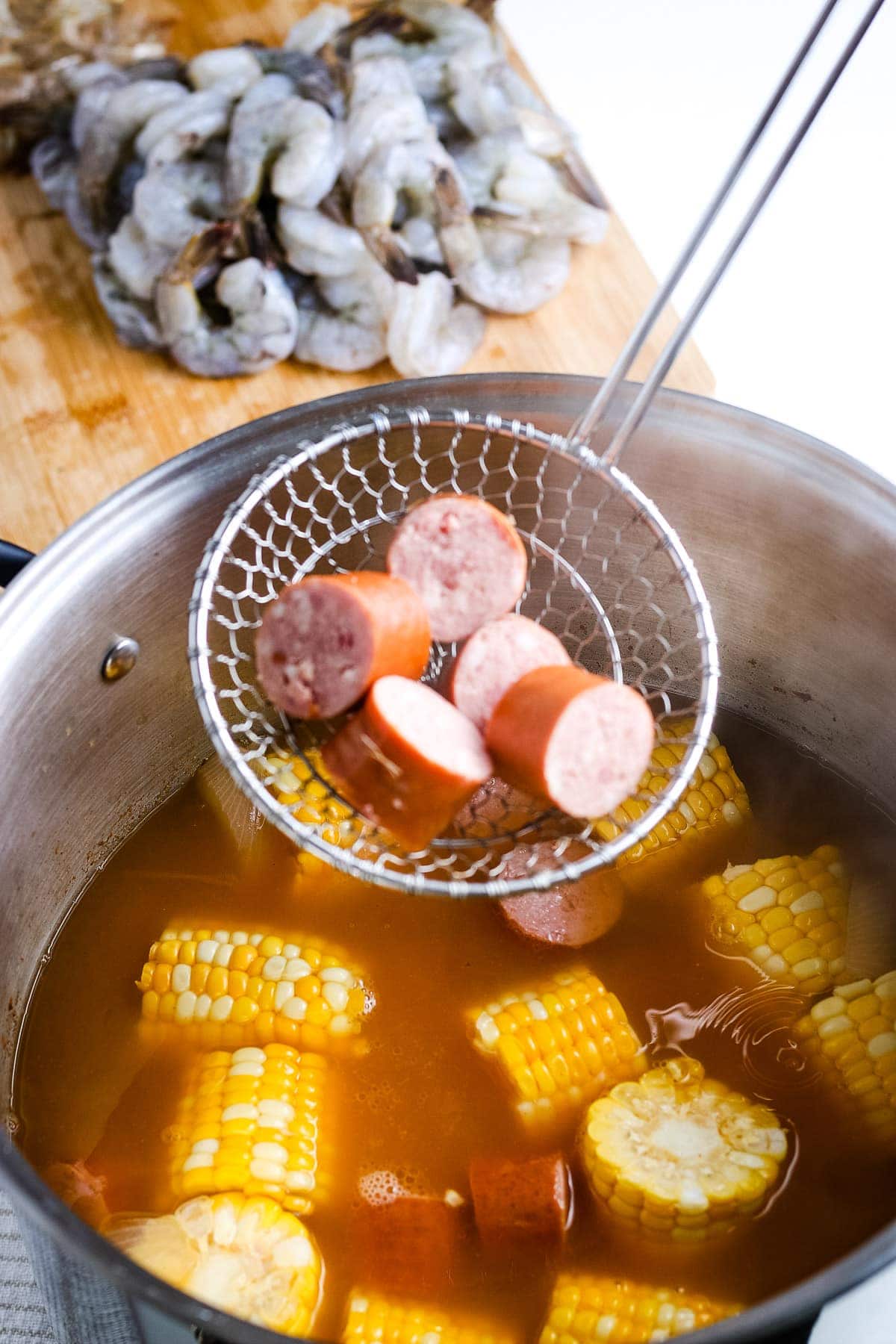 Ladle holding smoked sausage before placing it into shrimp boil pot