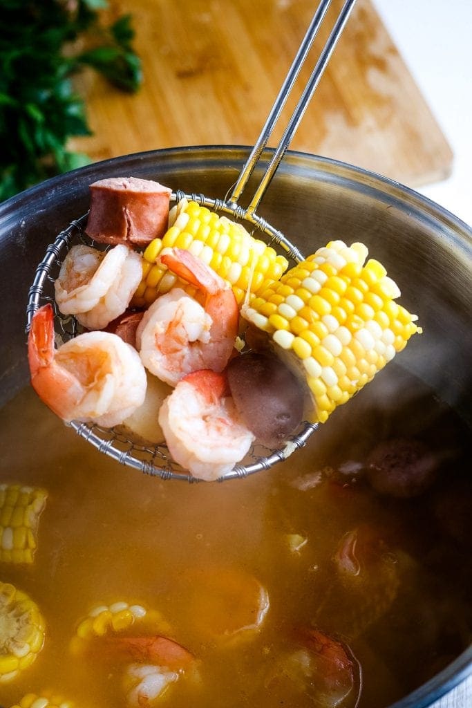 Ladle holding cooked shrimp, corn and sausage.