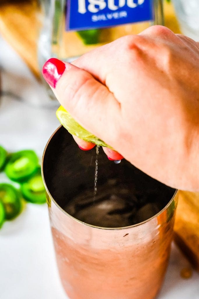 Hand squeezing fresh lime juice into a copper cocktail shaker.