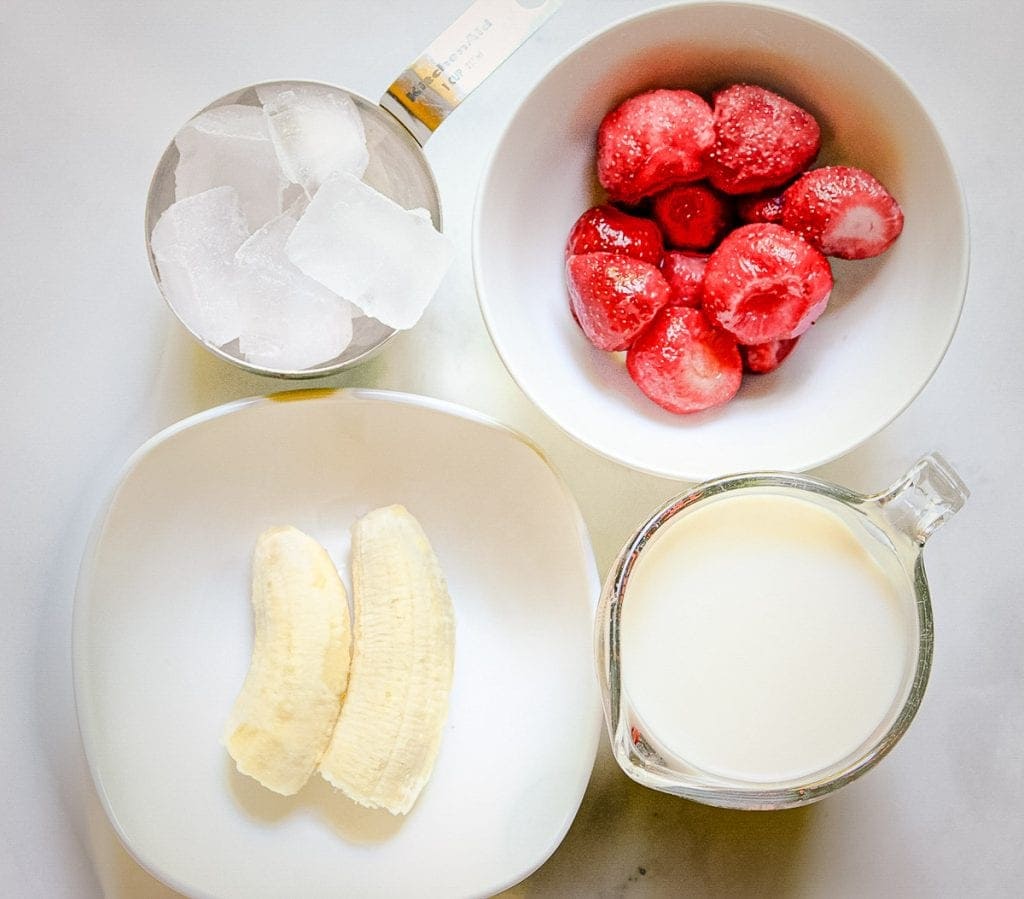 Overhead image of frozen strawberries, ice, banana and milk to make smoothie.