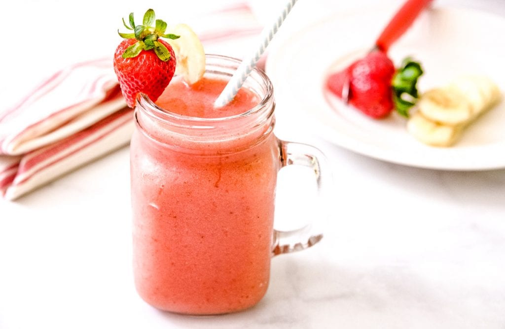 Marble background with a mason jar mug filled with Strawberry Banana Smoothie. A strawberry and banana slice on rim.