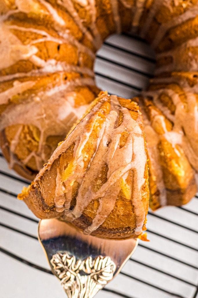 Overhead image showing a spatula taking a slice of zucchini bundt cake out of ring that's sitting on a wire rack.