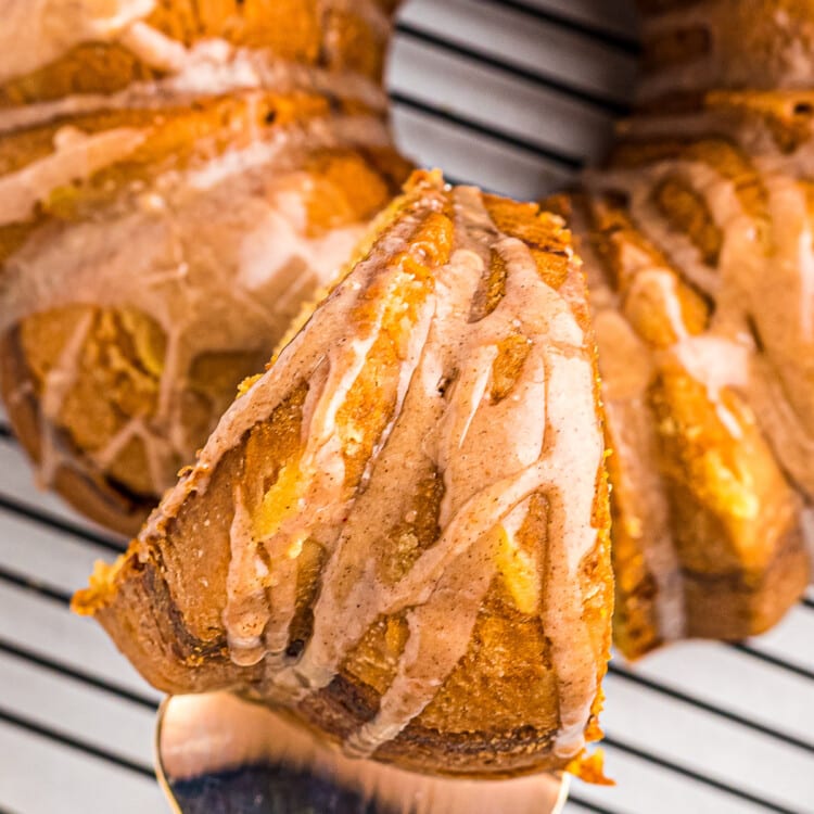 Overhead image showing a spatula taking a slice of zucchini bundt cake out of ring that's sitting on a wire rack.